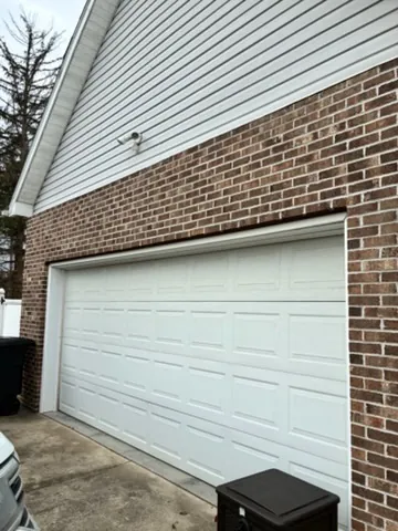 Warm Woodgrain on Brick garage before — A tired opening upgraded to warm woodgrain CHI doors that frame the brick.